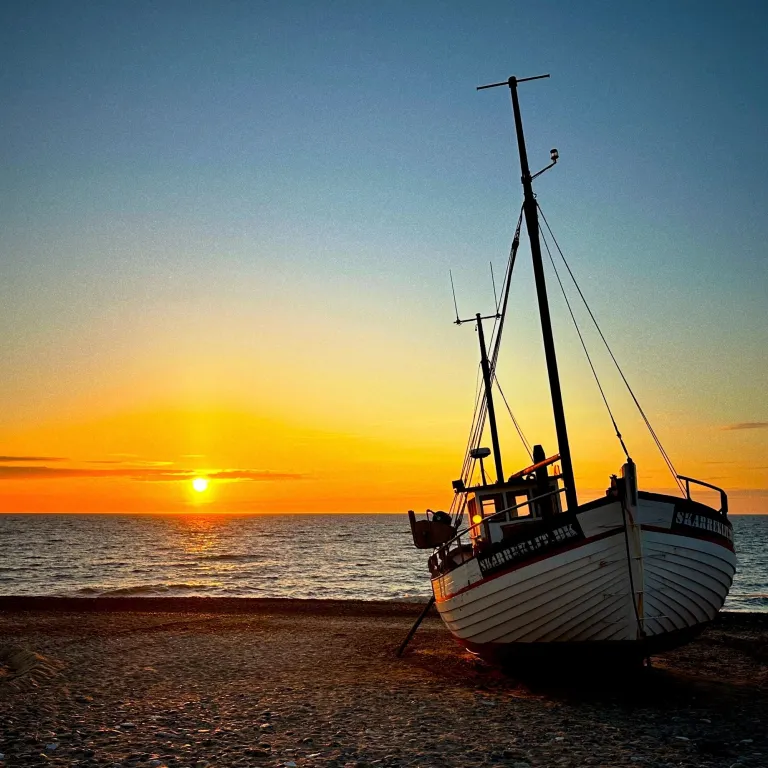 A fishing boat lying on the beach. In the background the sun is setting over the sea.