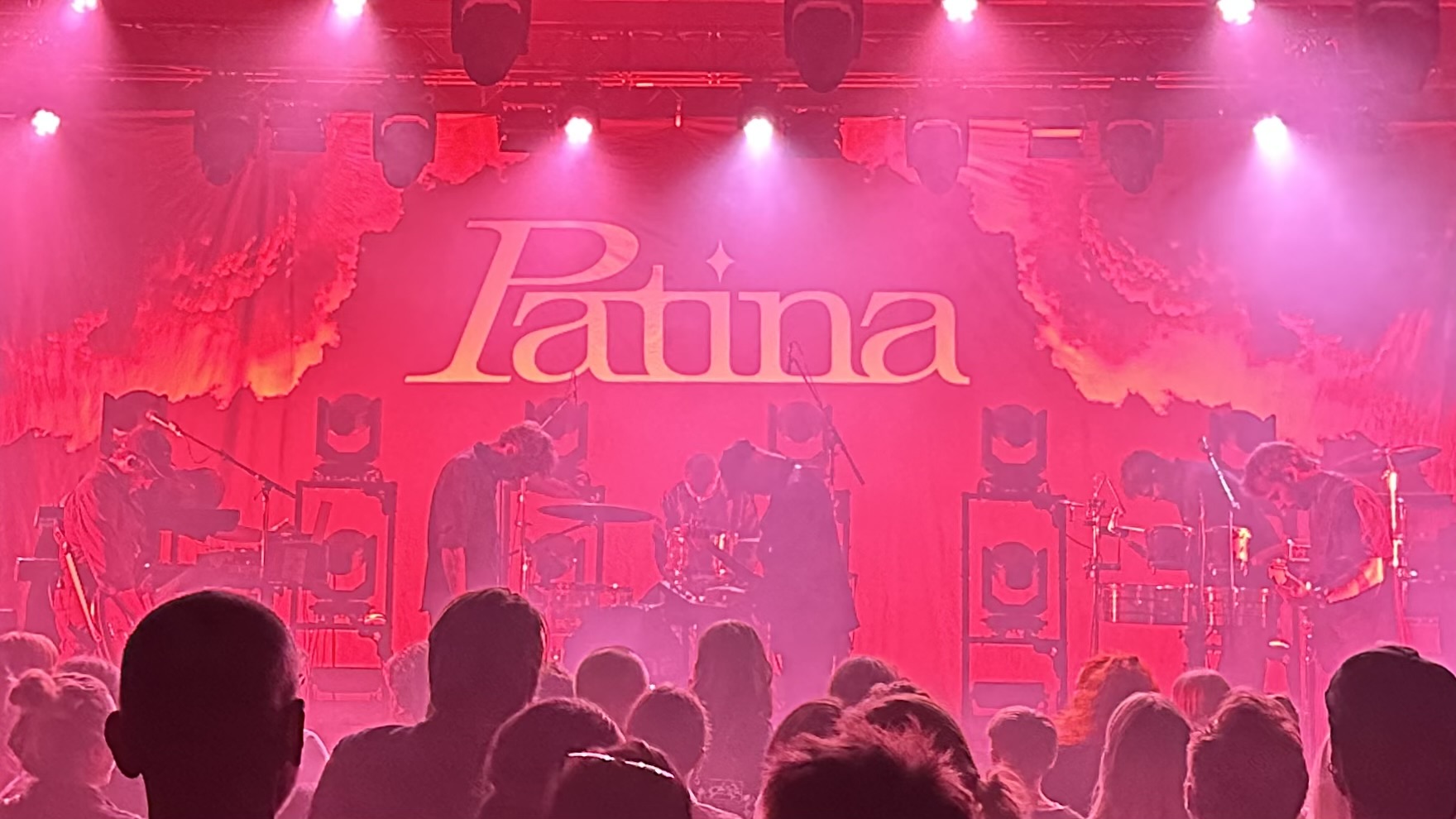 Scene med lys, røg og et band. På bagtæppet står der Patina med store bogstaver.